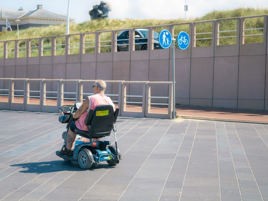 Pessoa idosa utilizando um scooter para mobilidade ao ar livre em ambiente urbano.