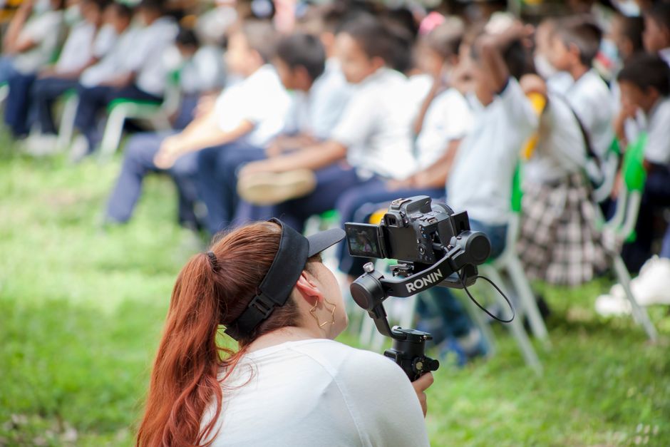 Fotógrafa capturando um evento com um grupo de crianças ao ar livre, em um ambiente escolar ou recreativo.