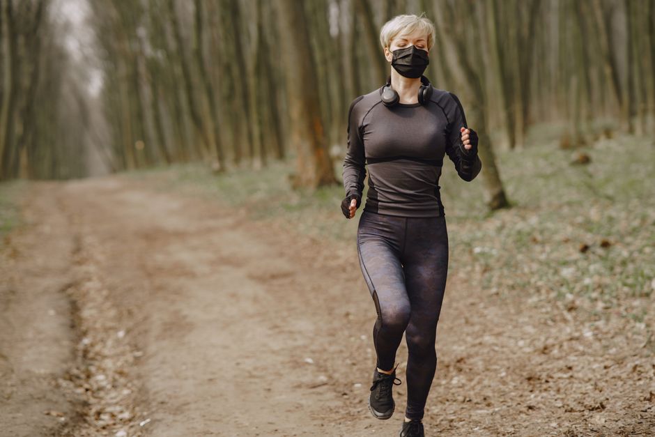 Mulher caminhando ao ar livre numa trilha na floresta, praticando exercício físico com máscara de proteção facial.