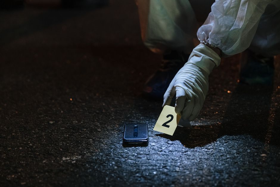 Imagem de uma investigação criminal onde uma pessoa com luvas descarta evidências na cena do crime à noite.