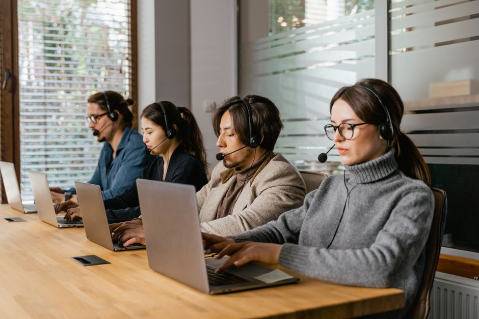 Equipe de atendimento ao cliente em call center com uso de computadores e headsets em ambiente de escritório moderno.