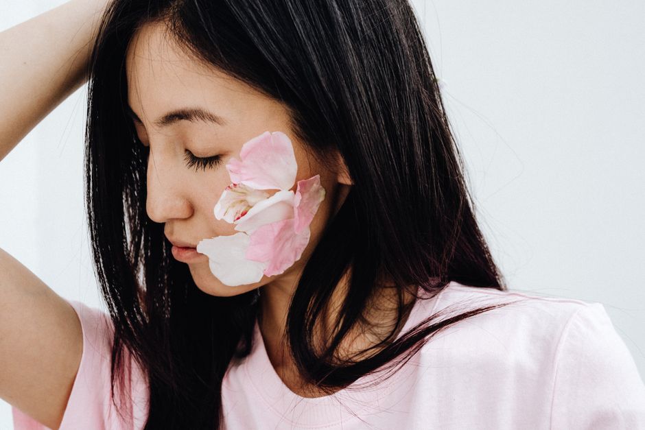 Mulher com expressão serena e delicada, com pétalas de flores na face, transmitindo uma atmosfera de tranquilidade e beleza natural.