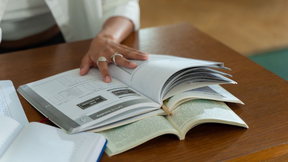 Pessoa revisando e organizando documentos e livros, simbolizando estudo ou pesquisa acadêmica.