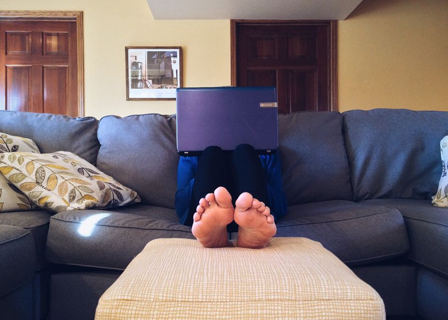 Pessoa descansando no sofá com um laptop na cabeça, em casa, transmitindo um momento de descontração ou descanso durante o trabalho ou estudo.