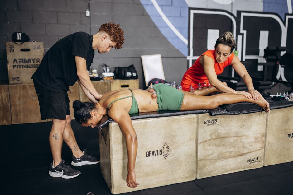 Duas terapeutas realizando uma sessão de cromo e terapia manual em uma mulher deitada em uma academia de treinamento funcional.