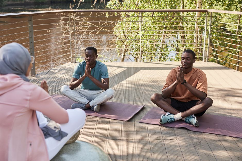 Homens participando de prática de meditação ao ar livre em um ambiente tranquilo com natureza ao fundo.