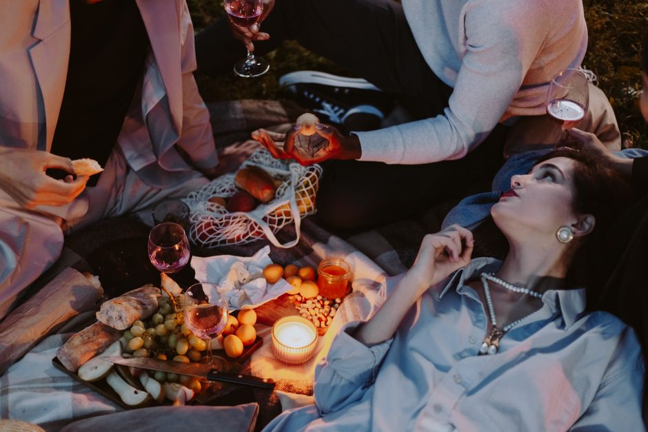 Um grupo de amigos celebra uma ocasião especial ao ar livre com comida, vinho e boa companhia ao entardecer.