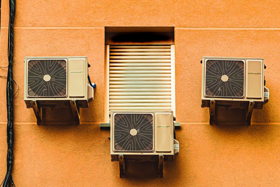 Imagem de três unidades de ar-condicionado instaladas em uma parede de cor laranja, simbolizando tecnologia e climatização de ambientes.