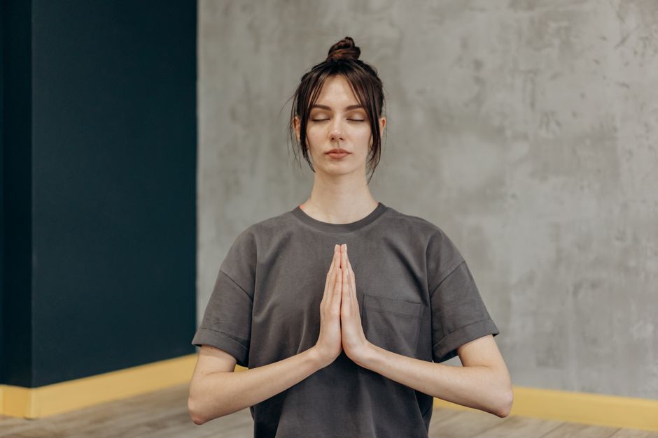 Mulher praticando meditação ou mindfulness em ambiente interno, com expressão de calma e concentração.