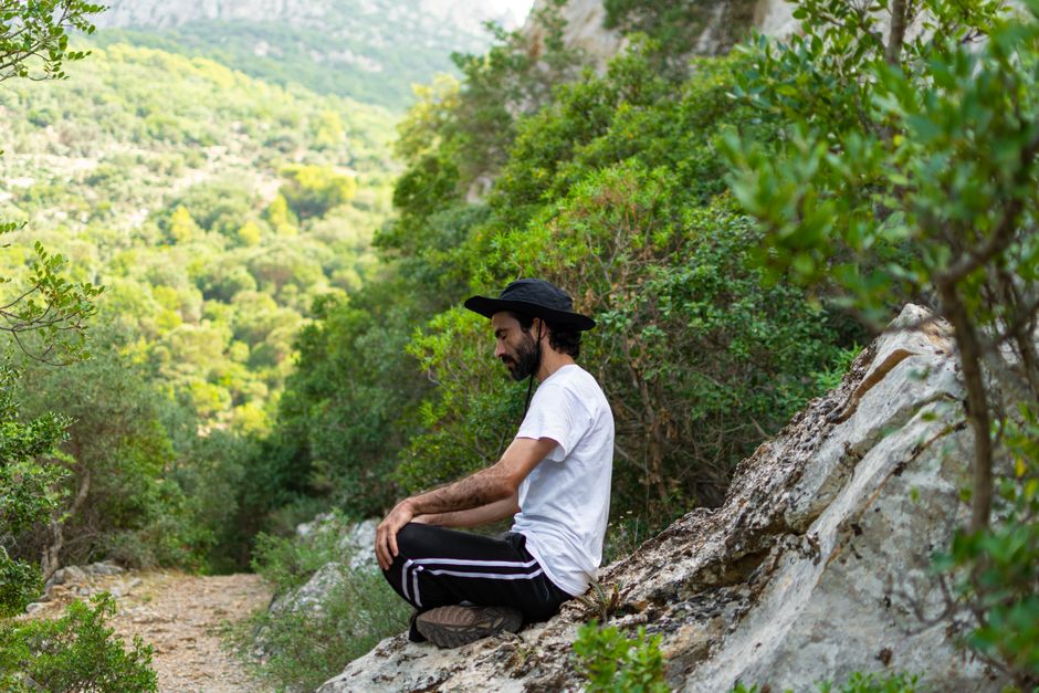 Homem meditando em meio à natureza, cercado por árvores e vegetação, em ambiente de tranquilidade e conexão com o meio ambiente.