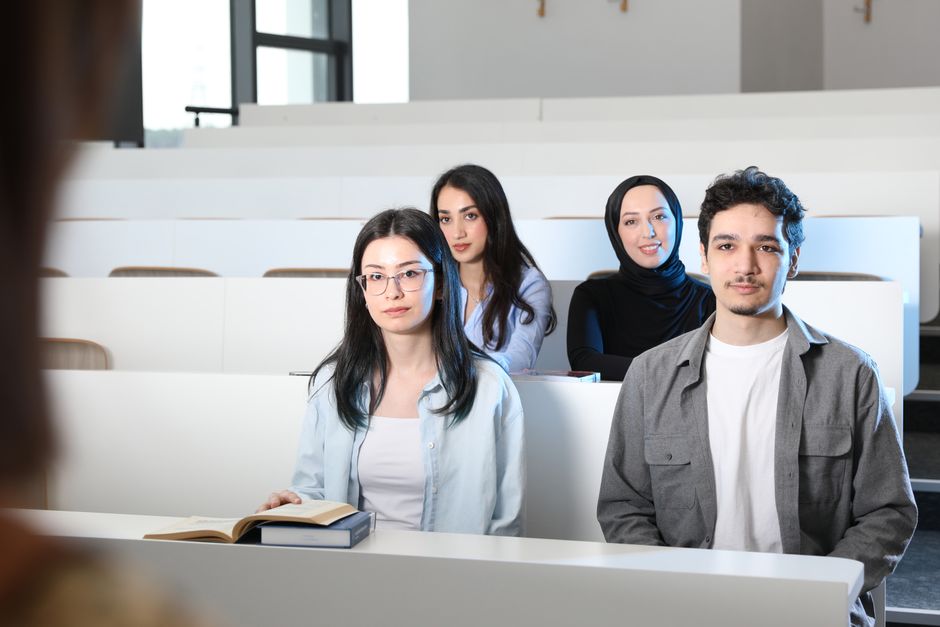 Grupo de estudantes em sala de aula, atentos durante uma aula ou palestra, em um ambiente acadêmico moderno.