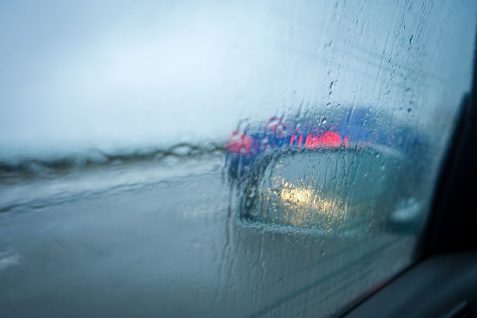 Imagem de uma janela embaçada pela chuva, com luzes de veículos ao fundo, transmitindo uma sensação de melancolia e reflexão durante uma tempestade.