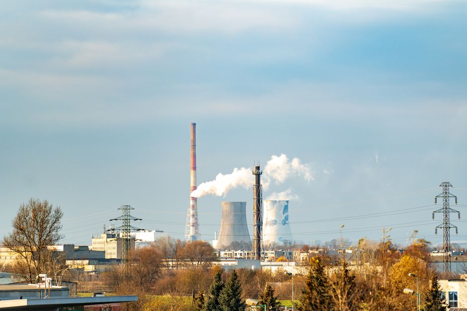 Vista de uma usina industrial com torres de resfriamento e fumaça saindo de sua chaminé, destacando o impacto da indústria na meio ambiente.