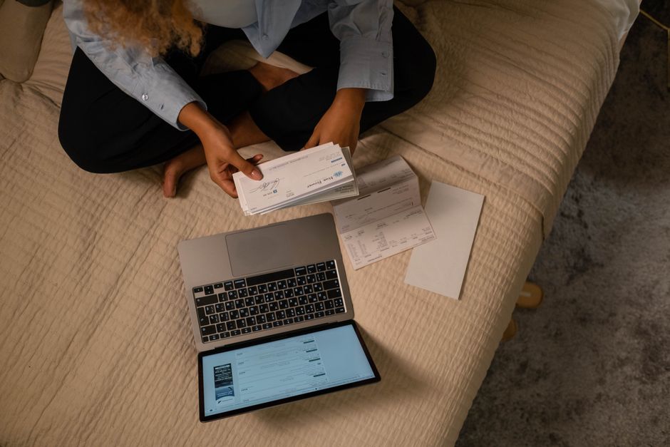 Pessoa organizando documentos financeiros em um ambiente doméstico com laptop e tablet, ilustrando planejamento financeiro ou administração pessoal.