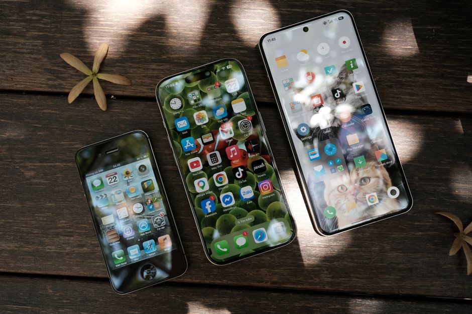 Imagem de três smartphones modernos posicionados sobre uma superfície de madeira, destacando o uso de dispositivos móveis na comunicação e tecnologia cotidiana.