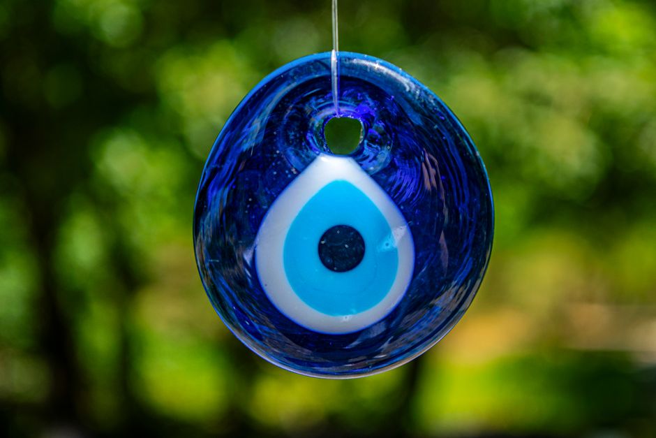 Cristal decorativo com símbolo do olho grego, representando proteção e espiritualidade, pendurado ao ar livre com fundo natural borrado.