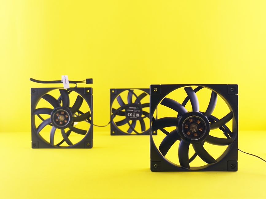 Três ventoinhas de computador conectadas por cabos em um fundo amarelo, representando tecnologia e refrigeração de sistemas eletrônicos.