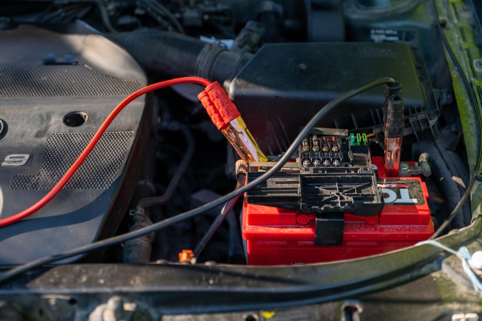 Imagem de um compartimento de carro com um procedimento de ligação de bateria, destacando a manutenção ou instalação elétrica veicular.