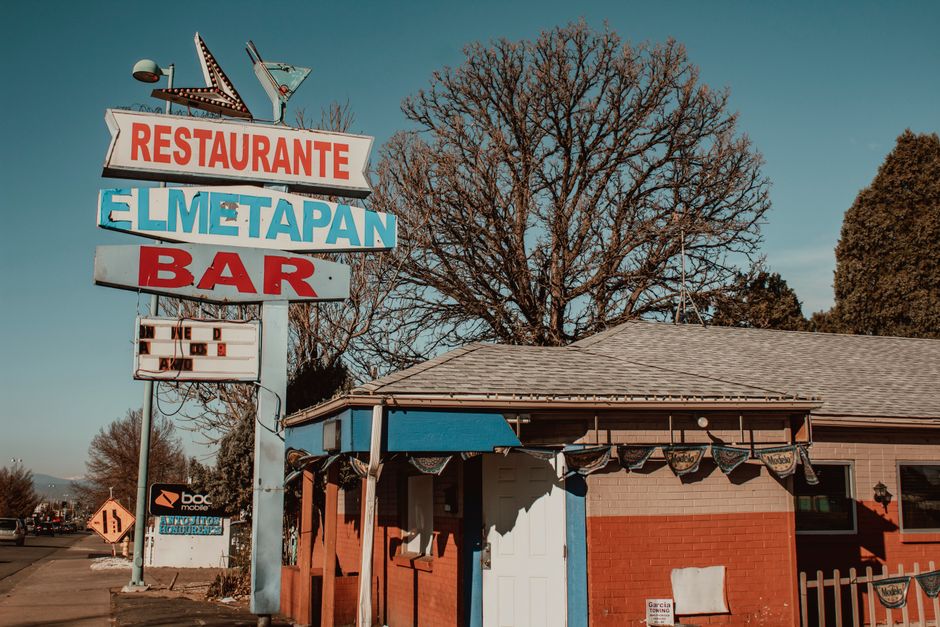 fachada de um restaurante e bar com sinais coloridos na frente de uma casa, em um ambiente urbano