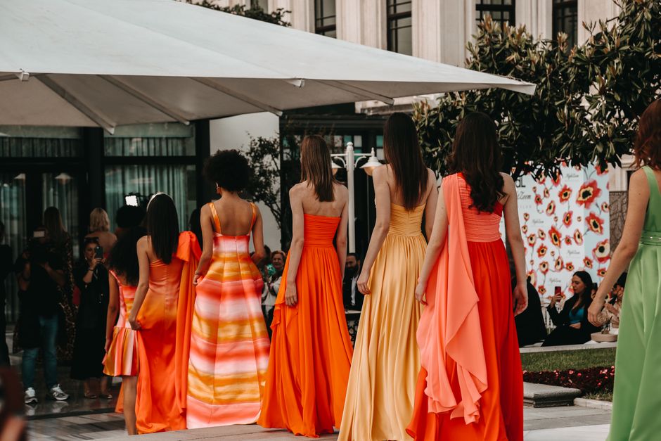 Modelos desfilando com vestidos elegantes em uma passarela ao ar livre, durante evento de moda ou desfile de roupas.
