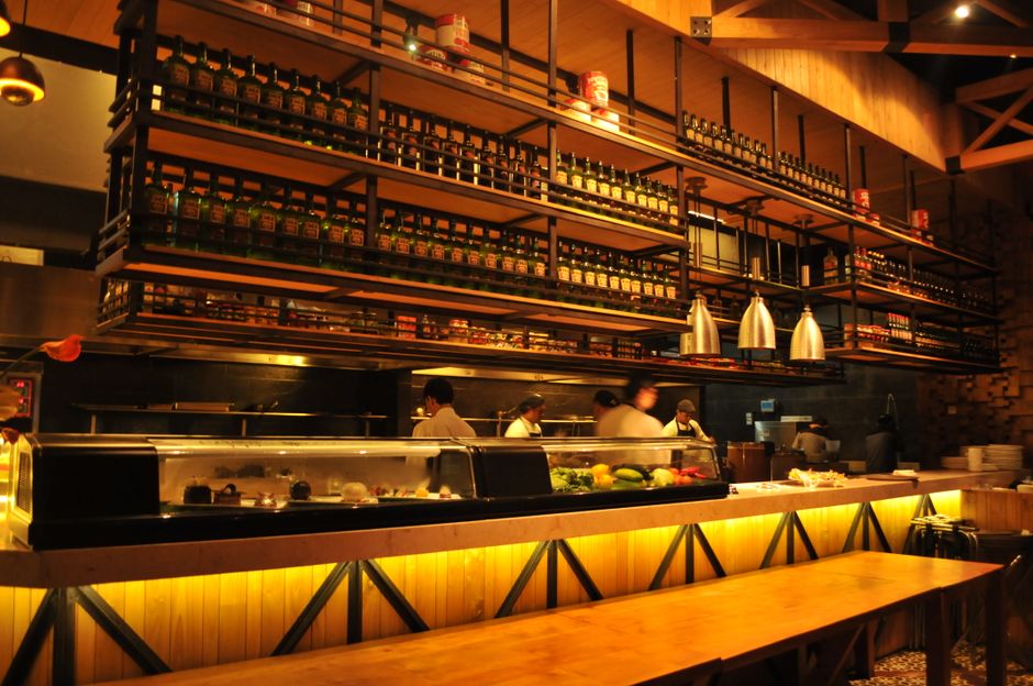 Imagem de um restaurante com equipe de cozinha preparando pratos, destacando um ambiente acolhedor e bem decorado.