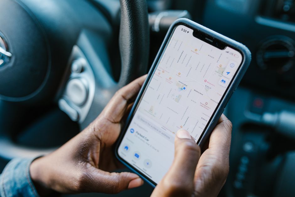 Pessoa utilizando um smartphone com aplicativo de navegação em um carro, indicando deslocamento ou viagem urbana.
