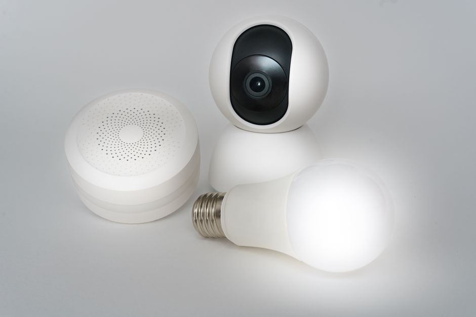 Imagem de dispositivos tecnológicos inteligentes, incluindo uma câmera de segurança, um sensor de presença e uma lâmpada LED, representando automação residencial.