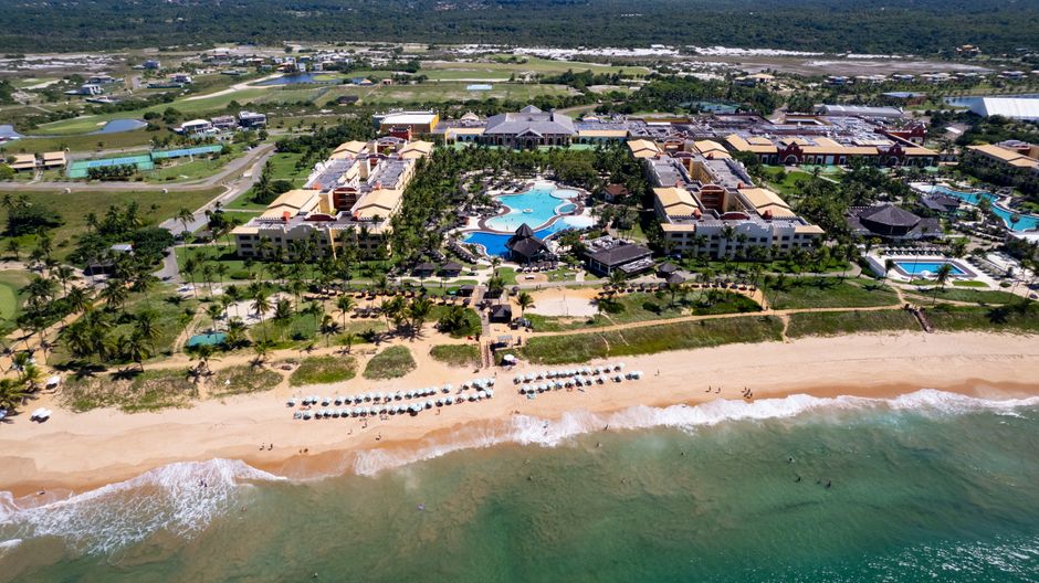 Imagem aérea de um resort à beira-mar com piscinas, áreas de lazer e espaço para atividades na praia, ideal para artigos sobre turismo e hospedagem de alto padrão.