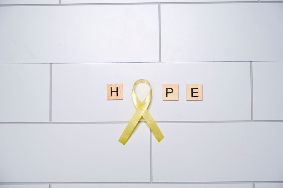 Imagem que transmite uma mensagem de esperança usando blocos de letras e um laço amarelo sobre uma parede branca.