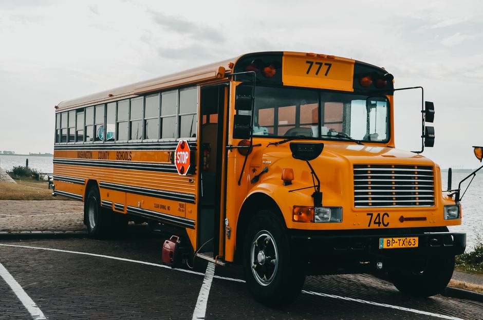 Imagem de um ônibus escolar amarelo estacionado com um cenário de céu nublado ao fundo, representando transporte institucional ou educação.