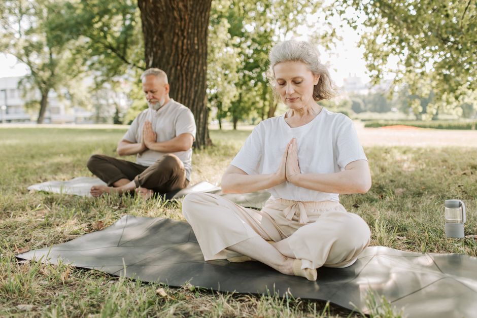 Duas pessoas praticando yoga ao ar livre em um parque, focando na mindfulness e bem-estar.