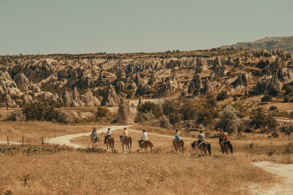 Grupo de pessoas fazendo passeio a cavalo em um cenário de paisagem de rochas e vegetação árida, típico de regiões turísticas ao ar livre.