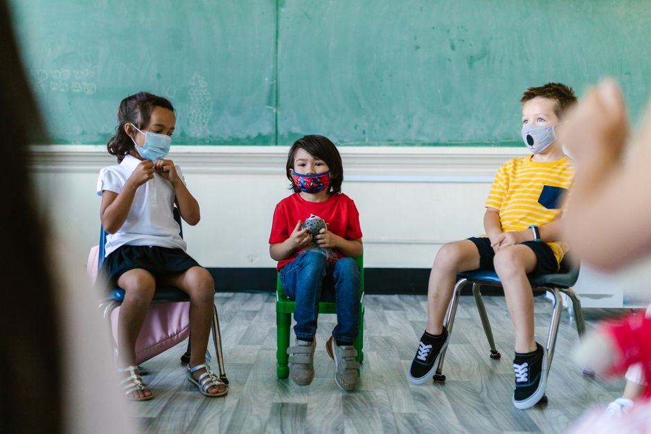 Crianças sentadas em uma sala de aula, usando máscaras, participando de uma atividade educativa ou interação social.