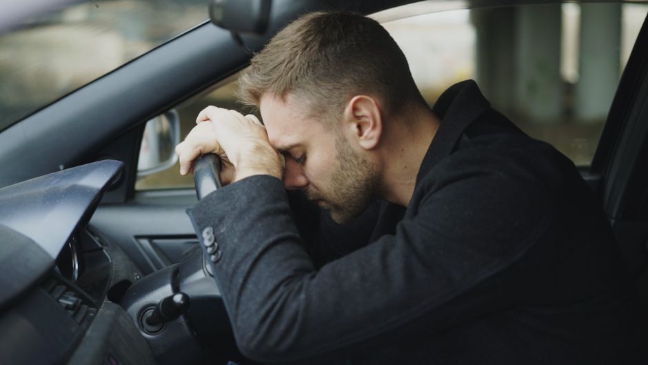 Homem triste e cansado dentro de um carro, transmitindo emoções de esgotamento ou frustração.