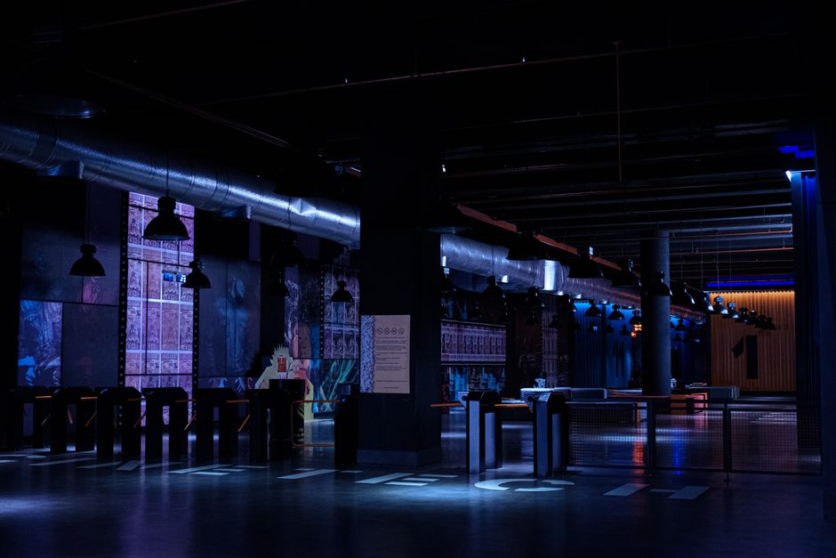 Espaço moderno e escuro, ideal para eventos de tecnologia ou entretenimento com iluminação ambiente rebaixada e elementos industriais.