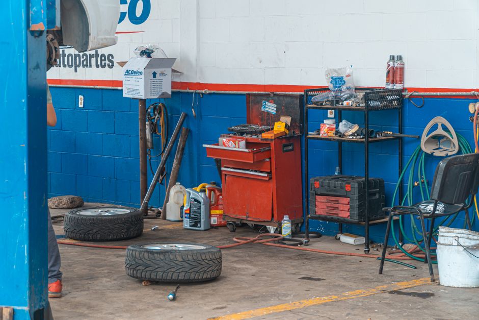 Imagem de uma área de oficina mecânica com ferramentas, pneus e equipamentos utilizados na manutenção veicular.