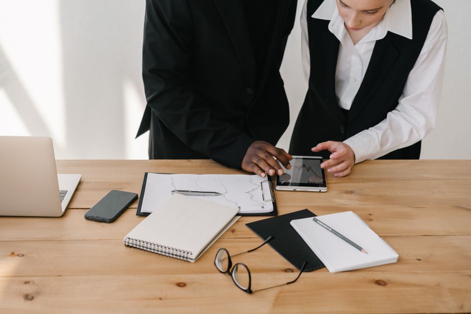 Duas pessoas de negócios analisando dados financeiros em um ambiente de escritório com tecnologia e documentos