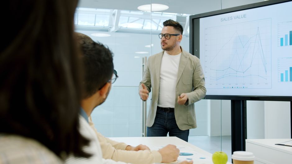 Homem apresentando gráficos de vendas em uma reunião de negócios moderna, focando em análise de desempenho e estratégias comerciais.
