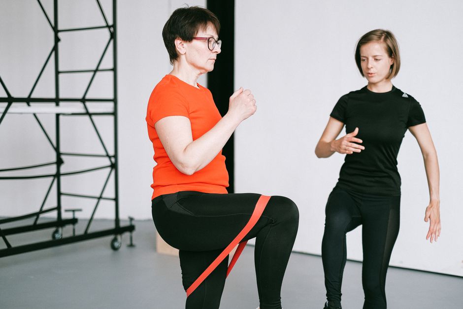 Duas mulheres realizando uma sessão de fisioterapia ou treino de reabilitação, com foco na perna e no fortalecimento muscular.