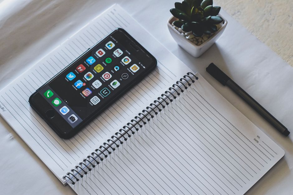 Imagem de um ambiente de trabalho com smartphone, caderno, caneta e uma planta suculenta, simbolizando produtividade e organização.