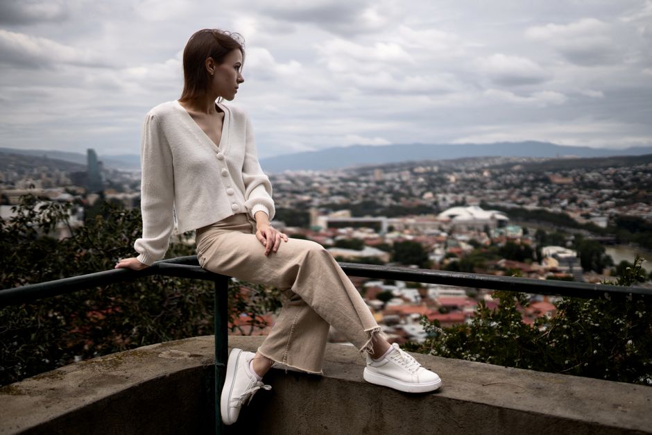 Mulher sentada relaxando em um ambiente ao ar livre, com vista panorâmica da cidade ao fundo, transmitindo sensação de contemplação e conexão com a natureza.