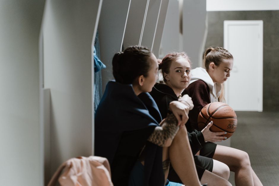 Garotas jovens aguardando antes de uma partida de basquete, mostrando momento de expectativa e preparação para o esporte.