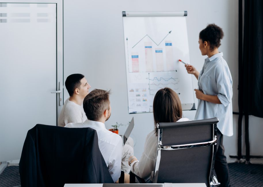 Multiprofissionais em reunião de apresentação de dados e análises estratégicas no contexto de negócios e gestão empresarial.