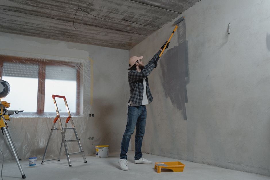 Pessoa pintando uma parede de uma sala em reforma ou construção, simbolizando modernização e renovação de ambientes.