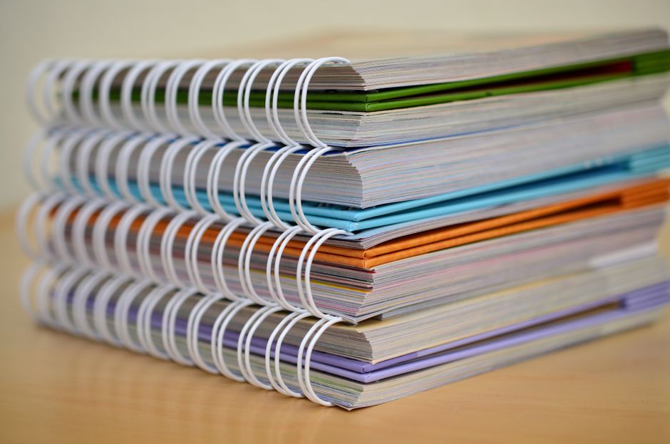 Pilhas de cadernos coloridos organizados em uma mesa, simbolizando estudo, pesquisa ou documentação detalhada.