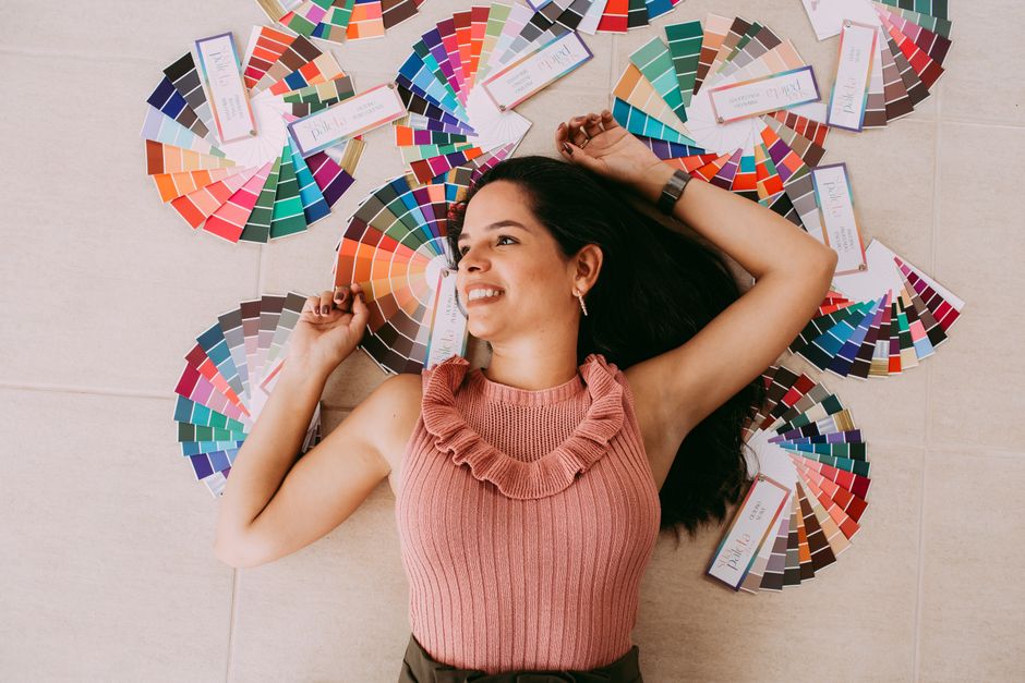 Mulher sorrindo deitada no chão cercada por paletas de cores, sugerindo criatividade e seleção de cores para design ou moda.