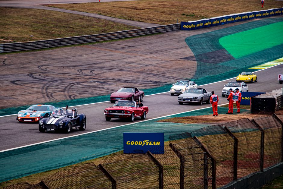 Carros de corrida em pista, com equipe de suporte ao lado, durante evento automobilístico.