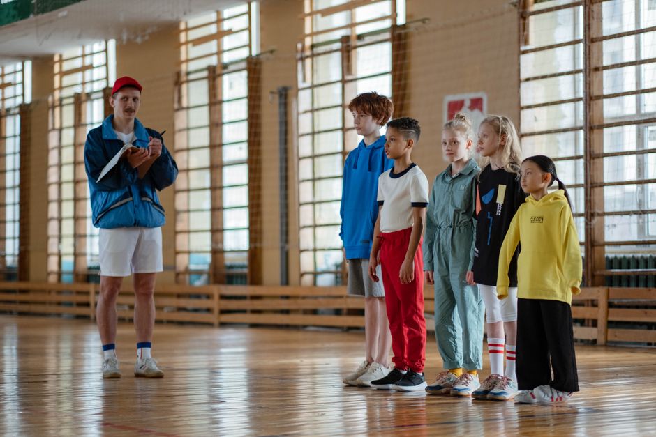 Instrutor ou treinador coordenando uma atividade com crianças em um ambiente esportivo indoor, focado em treinamento ou escolinhas de esporte.