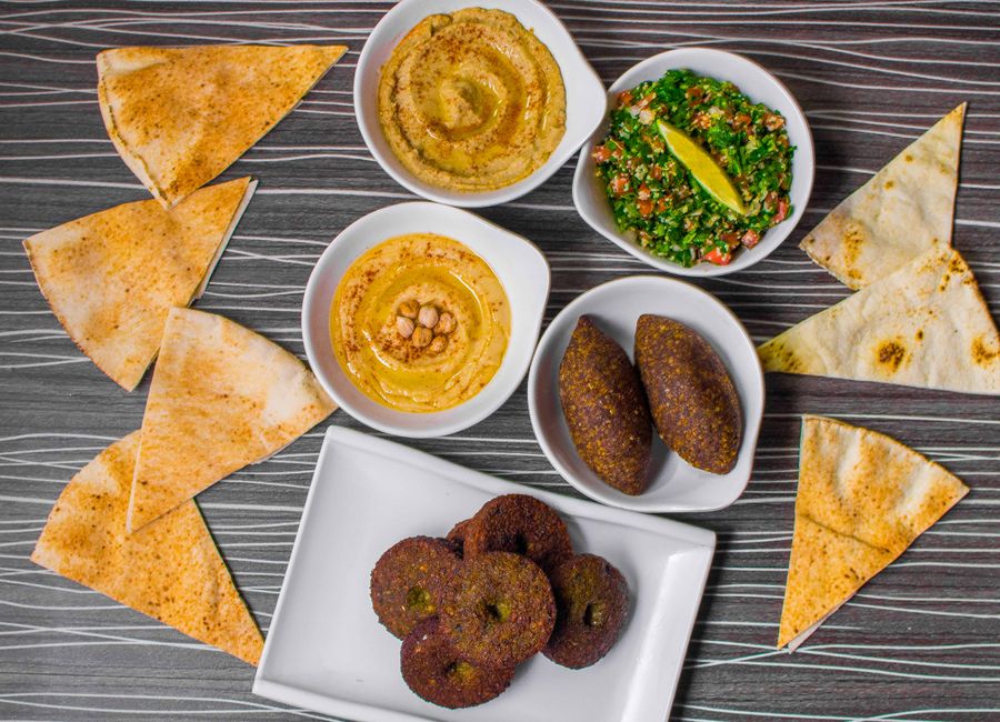 Imagem de uma variedade de pratos de comida típica do Oriente Médio, apresentando uma combinação de homus, babaganoush, kibe, falafel, pão sírio e salada de tabule, ideal para um artigo sobre gastronomia árabe ou culinária mediterrânea.