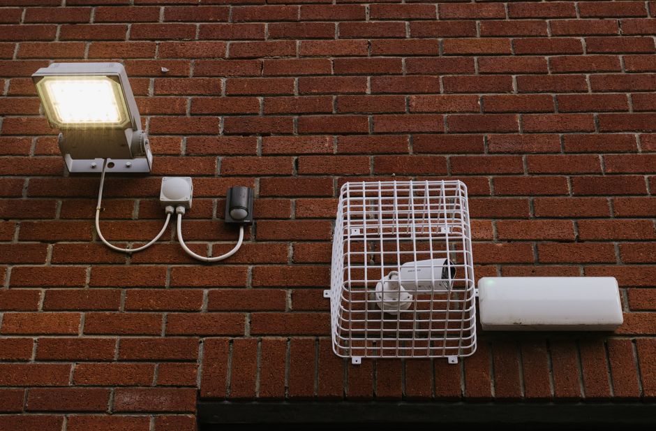 Iluminação externa com dispositivos de segurança instalados em uma parede de tijolos, destacando a tecnologia de proteção e controle de acesso.
